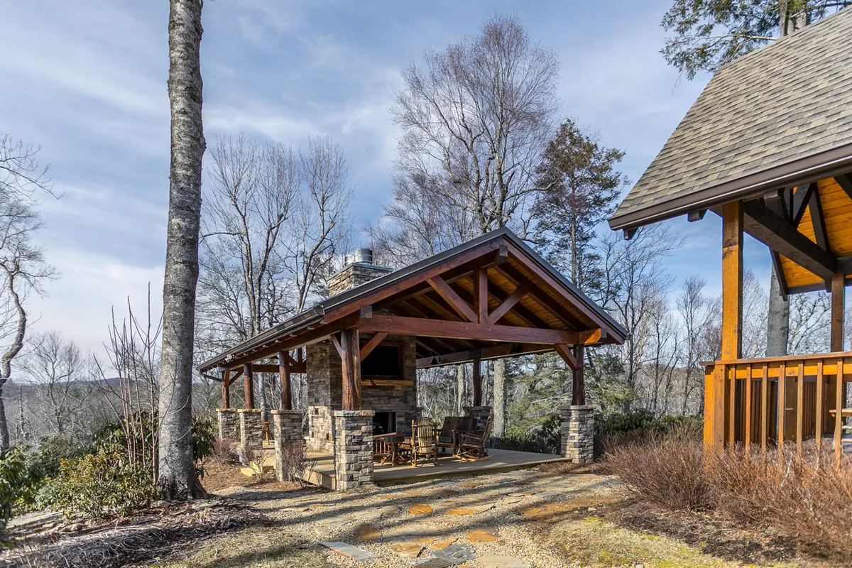 A cozy exterior gathering area featuring a wooden gazebo, a stone fireplace, and surrounding trees. The space is set up for outdoor gatherings, evening fireside chats, and enjoying the natural beauty, evoking the communal, social side of après-adventure life at the lodge.