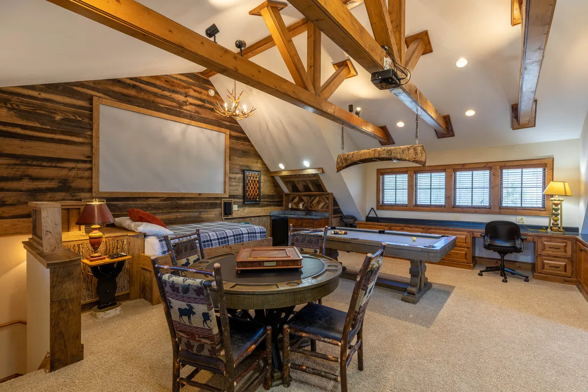 A spacious entertainment area featuring a pool table beneath exposed wooden beams, complemented by a round dining table for board games or socializing. The warm, inviting tones set the scene for family gatherings, game nights, and shared adventures.