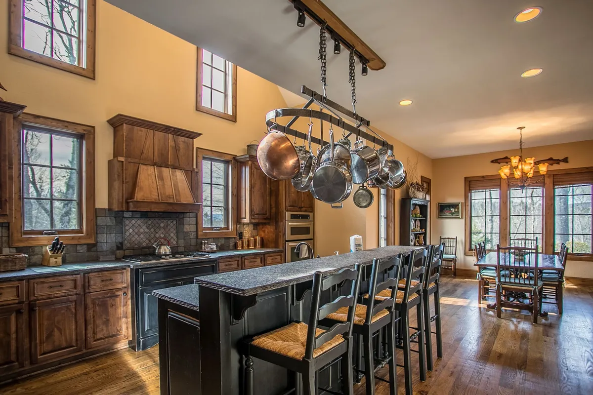 A large, open-concept kitchen is the focus, with a generous kitchen island, hanging pots, beautiful wooden cabinetry, and expansive windows. The space is both functional and welcoming, perfect for preparing meals or gathering with family and friends.