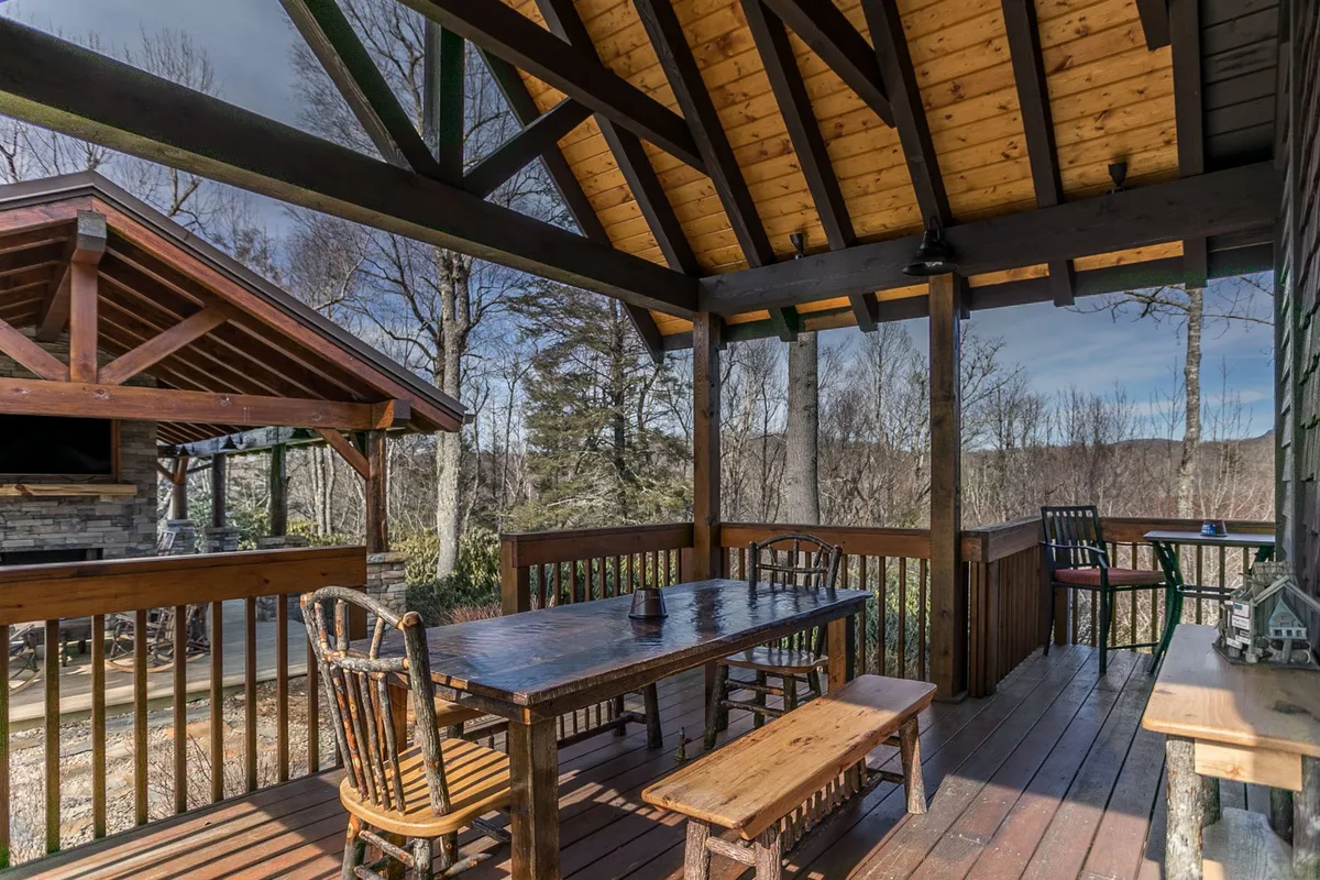 A rustic wooden dining table with chairs is surrounded by trees and landscape views, set on an outdoor patio or deck. The setup is ideal for group dining, evening conversations, and enjoying scenic sunsets together.