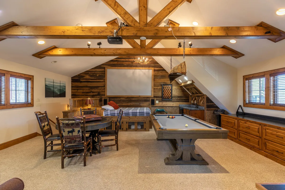 A relaxed, friendly space featuring a pool table, dining table, and a cushioned seating area. The wooden beams add a rustic touch, making it ideal for both casual games and cozy movie nights with friends or family.