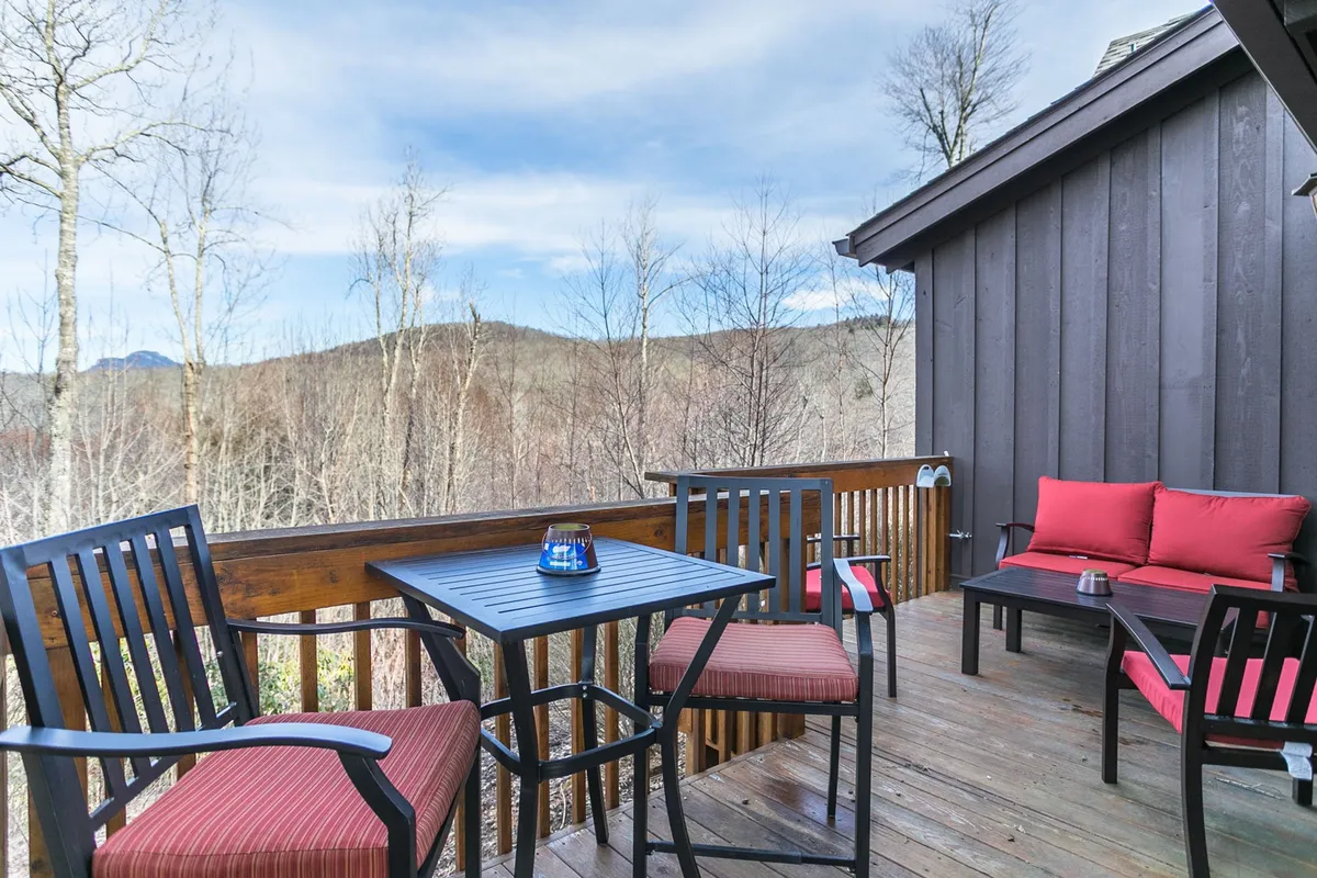 A tranquil wooden deck with comfortable red-cushioned seating overlooks expansive mountain views. The open deck is surrounded by nature, making it an ideal spot for relaxing, socializing, or enjoying a drink while taking in sunrise or stargazing at night.