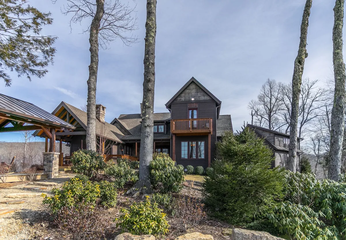 This exterior shot captures the large wooden house set against tall trees and a landscaped garden, with an inviting outdoor gazebo. The scene suggests ample space for group activities and relaxation, echoing the lodge's promise of both adventure and retreat.