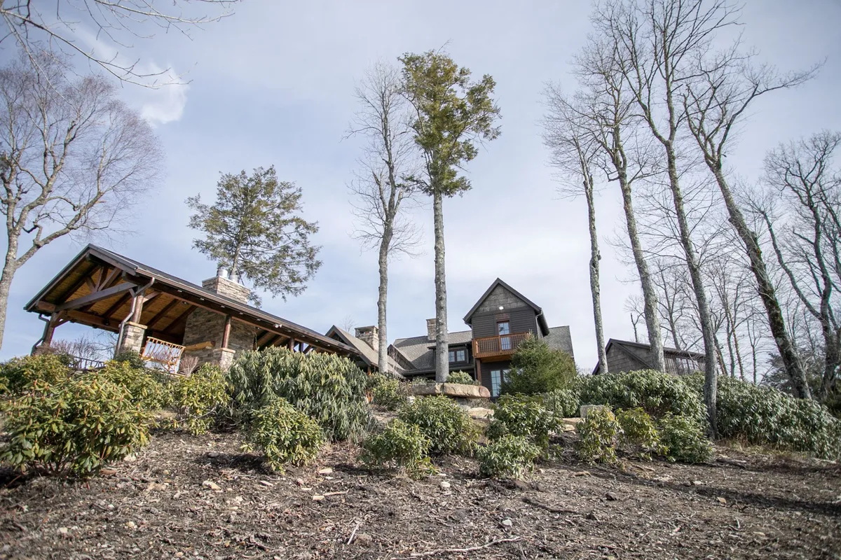 This image captures the inviting exterior of Elk Camp Lodge, set amidst lush greenery with the main house and an outdoor structure visible. The landscaped surroundings and seating arrangements suggest a perfect environment for family gatherings, outdoor dining, and shared relaxation in a serene natural setting.