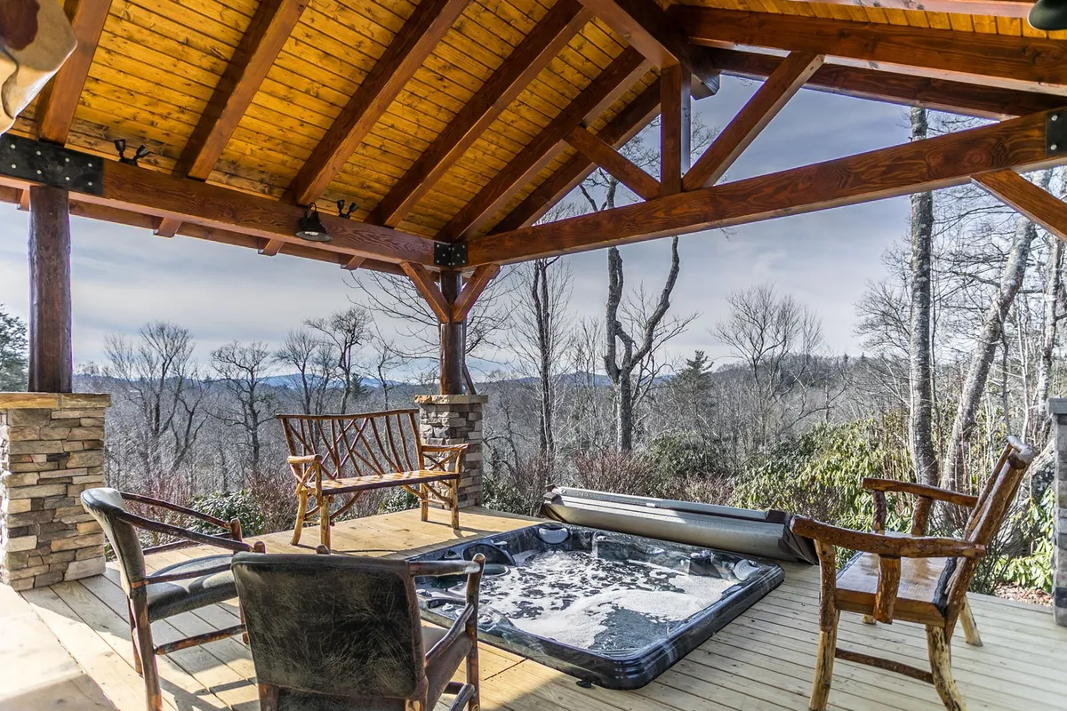 An outdoor hot tub nestled under wooden beams with a scenic view beyond, surrounded by chairs for relaxation. The setting invites guests to unwind after adventurous days, with a sense of tranquility and immersion in nature as the sun sets or stars appear overhead.